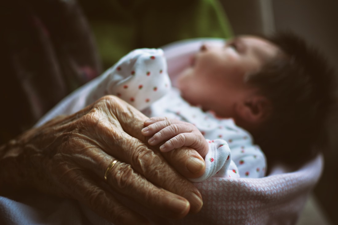 Hand einer Seniorin hält ein Baby – Symbolbild